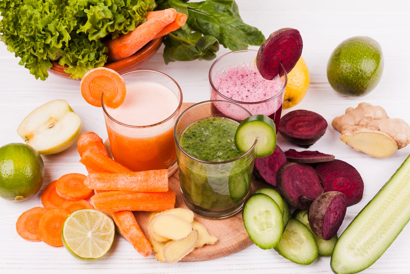 Mesa blanca con vasos de jugo con diferentes aportes al cuerpo, con distintas verduras como zanahorias, pepino y betabel.