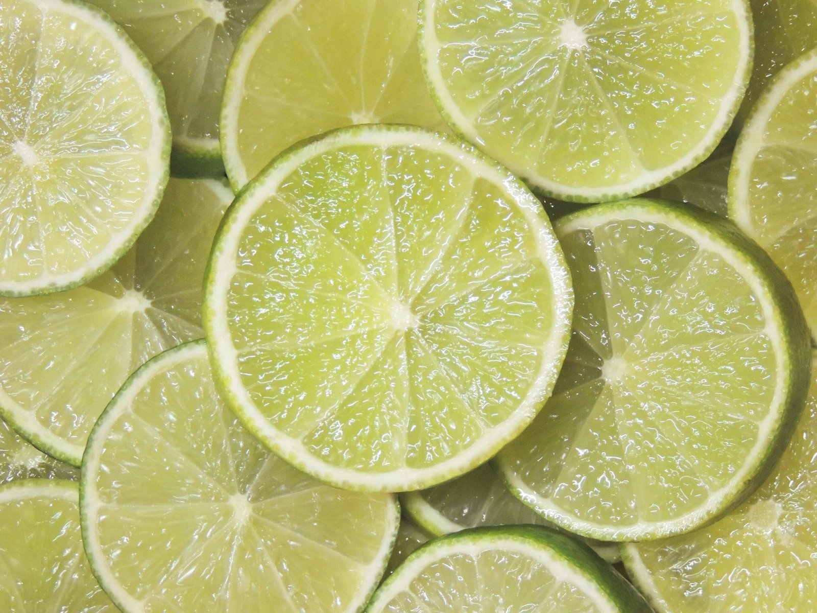 Un primer plano detallado de múltiples rodajas de limón verde superpuestas, mostrando la textura de la pulpa y la cáscara.